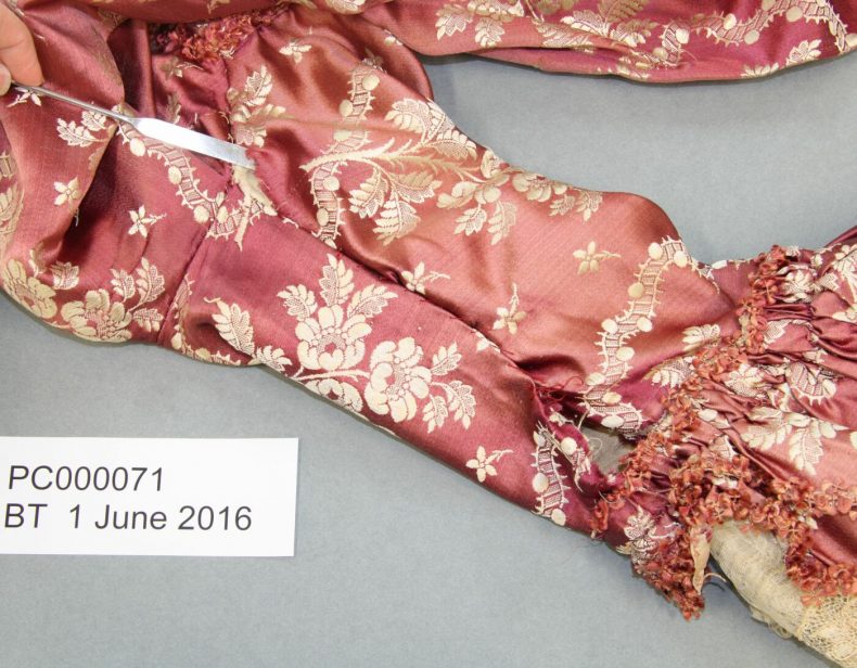 PC000071 proper right sleeve seam, showing previous repairs and fading of the silk. Photo by A. Peranteau, copyright Te Papa.